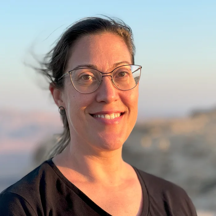 שירי פלס, מטפלת וואטסו מוסמכת, מחייכת אל המצלמה על רקע נוף בשעת שקיעה